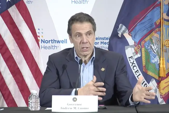 Governor Andrew Cuomo speaks to reporters seated at a table in a Long Island laboratory.